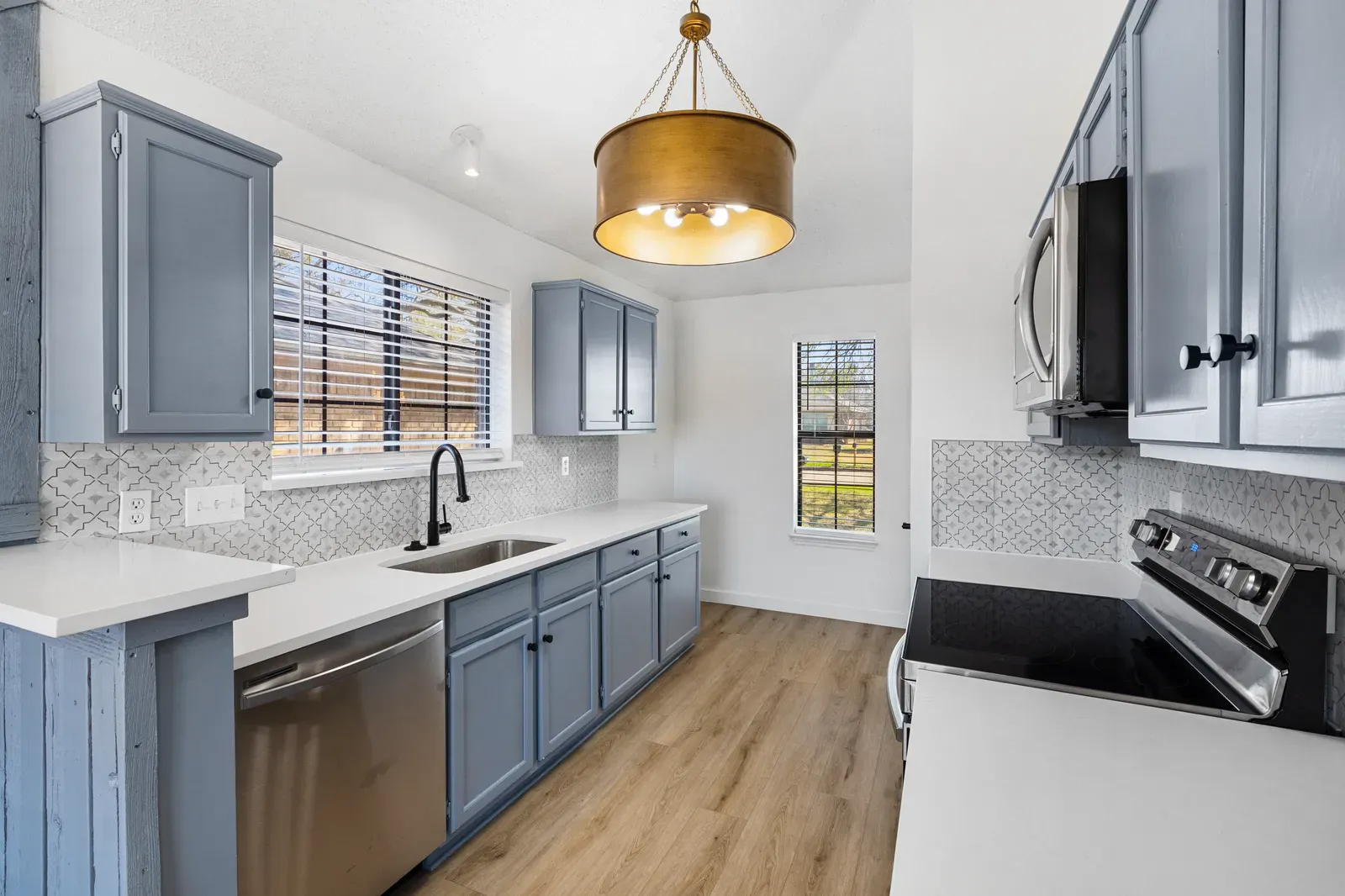 Bianco quartz countertops on blue-gray cabinets with a brass pendant in Allen, TX