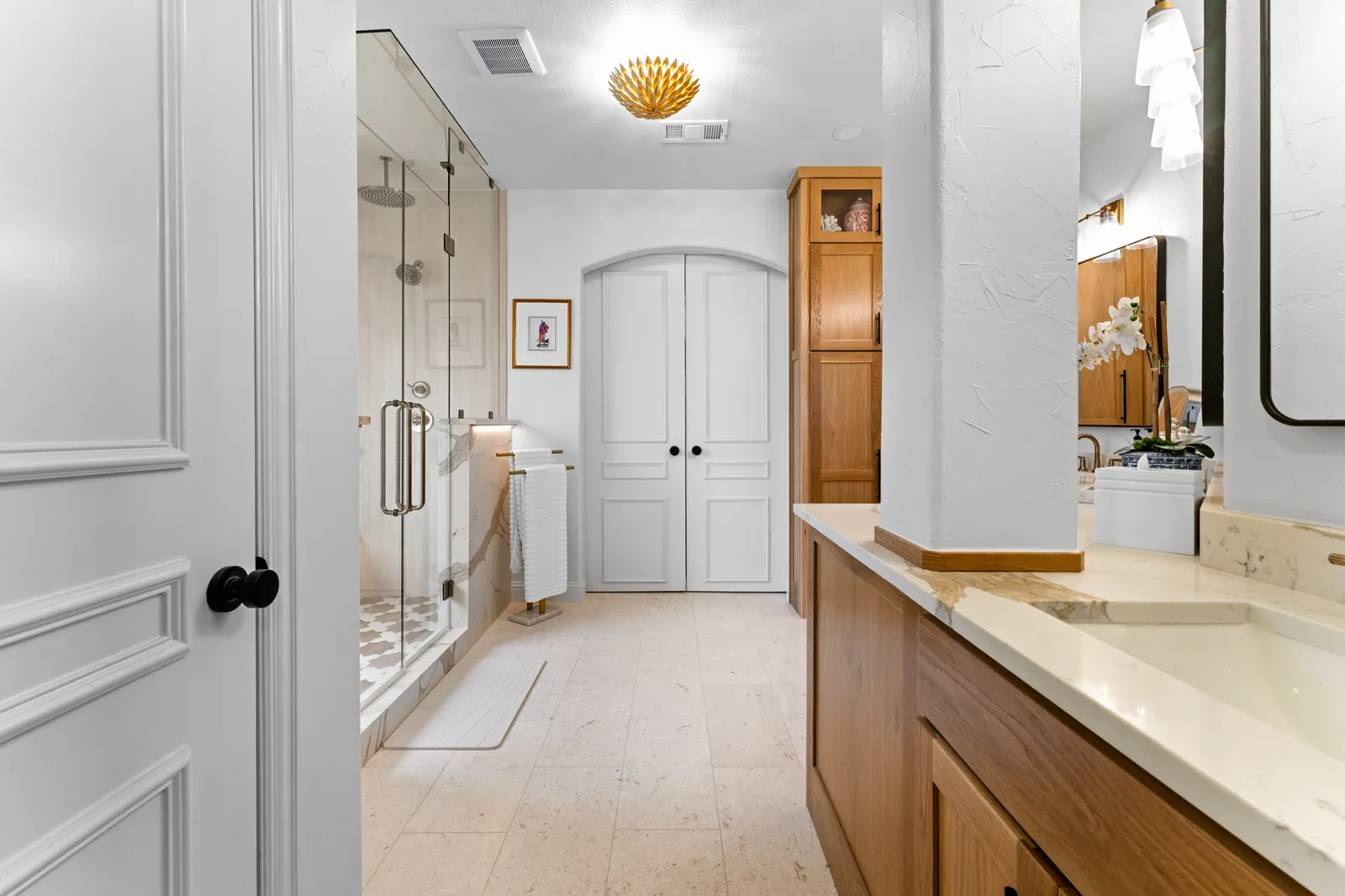 Long quartzite vanity run with a glass shower and arched doors in a Plano, TX primary bathroom