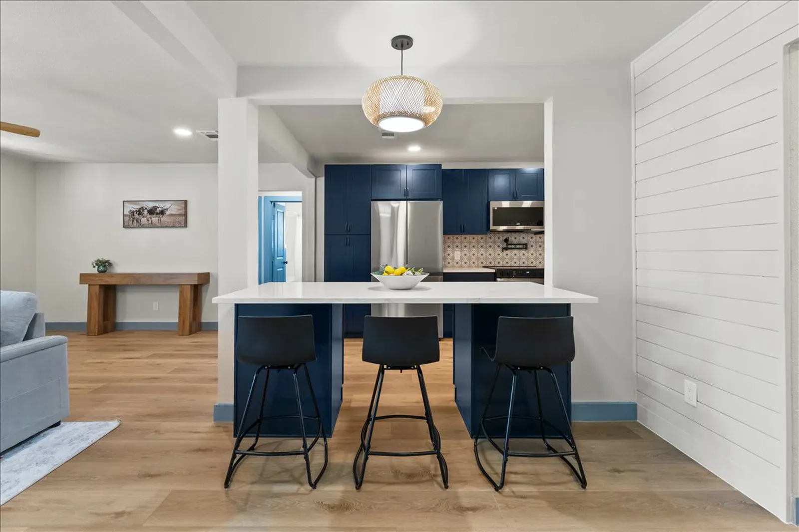 Bianco quartz island with seating and a rattan pendant in a navy kitchen in McKinney, TX