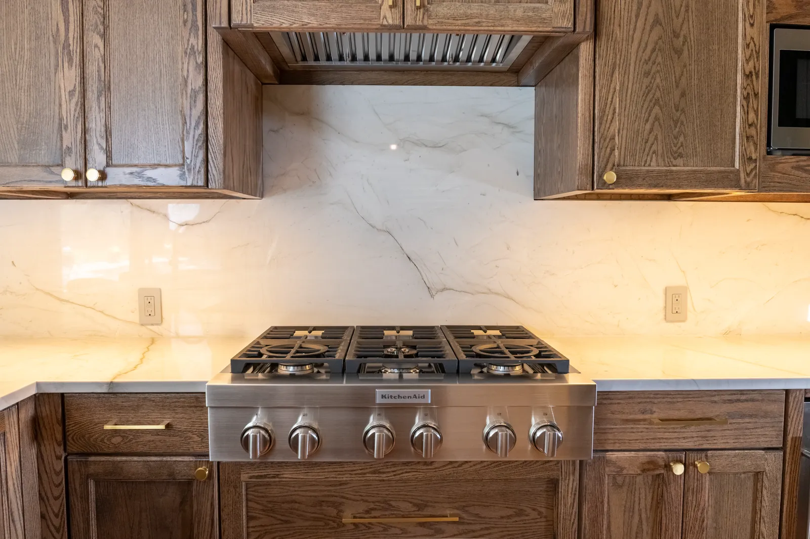 Full-height quartzite slab backsplash, matching the counters, behind a gas range with oak cabinetry in a Preston Hollow, Dallas kitchen